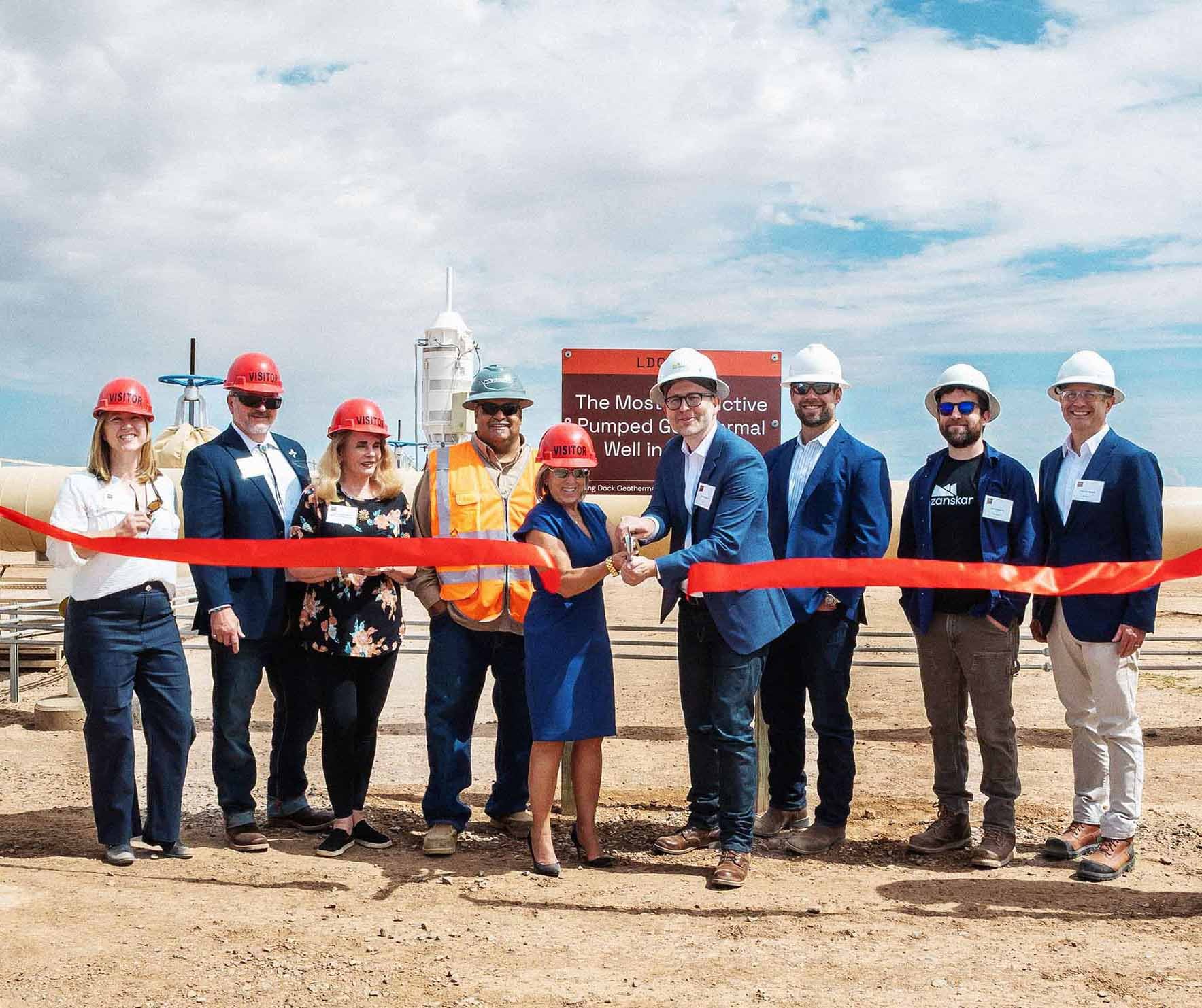 Group of Zanskar team members, partners, and officials including Governor Michelle Lujan Grisham cutting a red ribbon in front of Lightning Dock Geothermal Power Plant in New Mexico. Participants wear hard hats and safety gear, marking the official opening of the site.