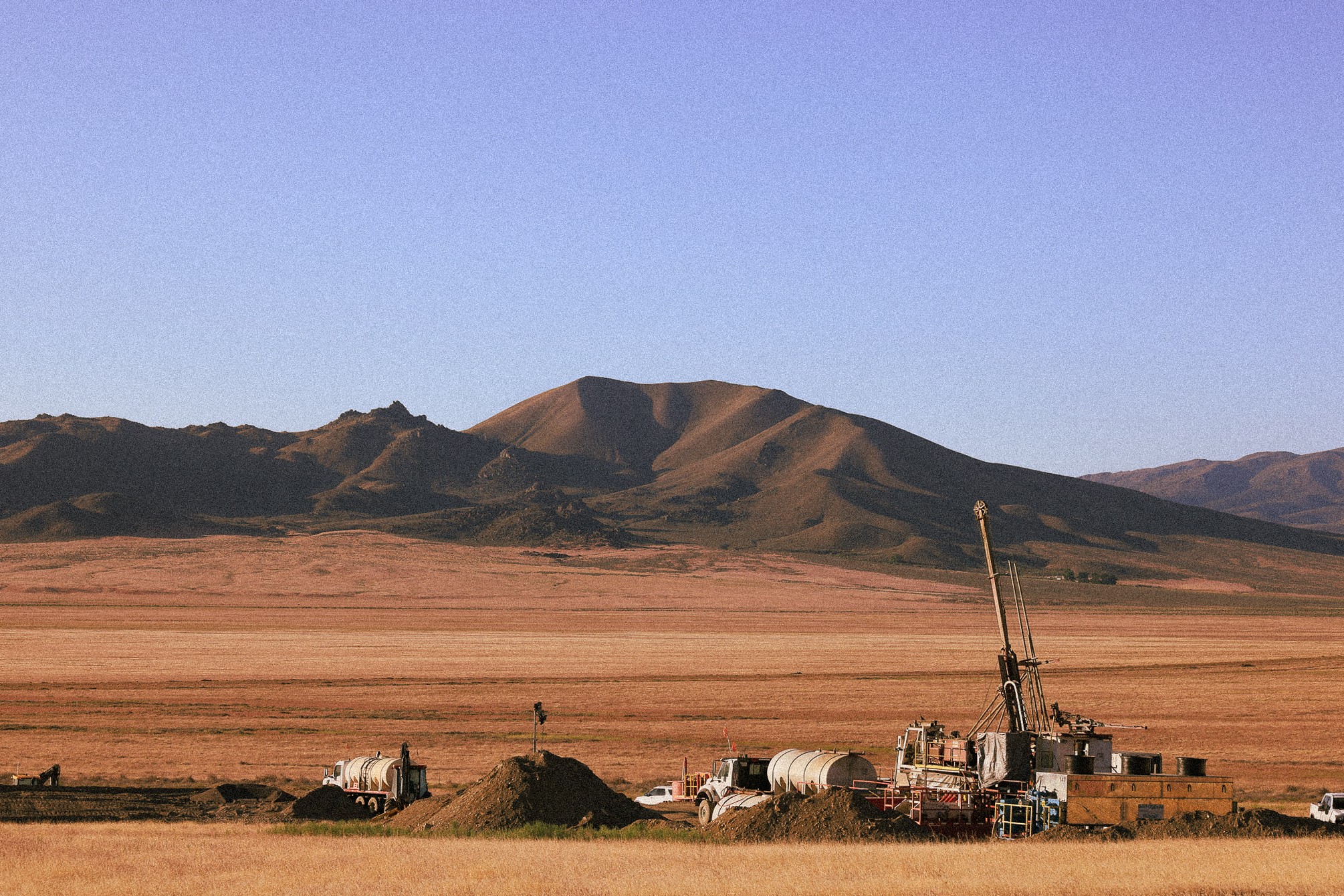 Drilling rigs and trucks operating on a desert plain with a large mountain range in the background, representing geothermal exploration and future projects underway.